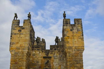 Majestic medieval stone castle fortress featuring ancient defense walls, battlements, and tall towers surrounded by green grass under a cloudy sky. Alnwick castle England, towers a very old castle © TomKorcak