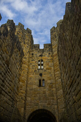 Majestic medieval stone castle fortress featuring ancient defense walls, battlements, and tall towers surrounded by green grass under a cloudy sky. Alnwick castle England, towers a very old castle © TomKorcak