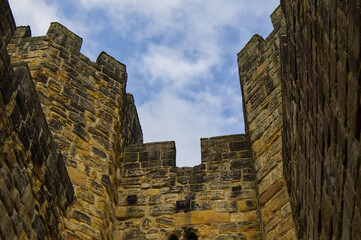 Majestic medieval stone castle fortress featuring ancient defense walls, battlements, and tall towers surrounded by green grass under a cloudy sky. Alnwick castle England, towers a very old castle © TomKorcak