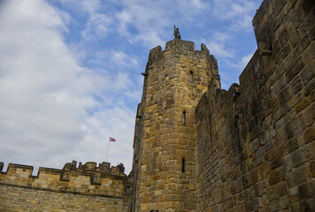 Majestic medieval stone castle fortress featuring ancient defense walls, battlements, and tall towers surrounded by green grass under a cloudy sky. Alnwick castle England, towers a very old castle © TomKorcak
