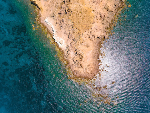 Drone aerial top down view of rocky Cape Akrotiri tip and turquoise sea in Santorini Greece
