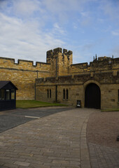 Majestic medieval stone castle fortress featuring ancient defense walls, battlements, and tall towers surrounded by green grass under a cloudy sky. Alnwick castle England, towers a very old castle © TomKorcak