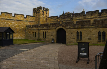 Majestic medieval stone castle fortress featuring ancient defense walls, battlements, and tall towers surrounded by green grass under a cloudy sky. Alnwick castle England, towers a very old castle © TomKorcak