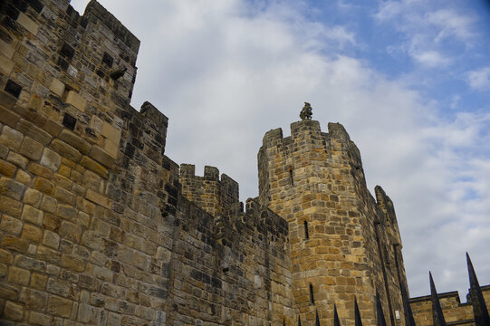 Majestic medieval stone castle fortress featuring ancient defense walls, battlements, and tall towers surrounded by green grass under a cloudy sky. Alnwick castle England, towers a very old castle