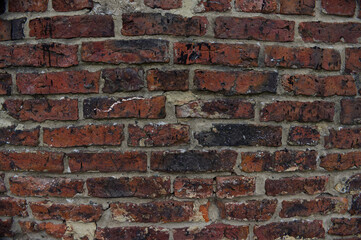 Fototapeta premium Old red weathered brick wall texture with dark grunge spots and crumbling mortar. Rustic industrial architecture background pattern.