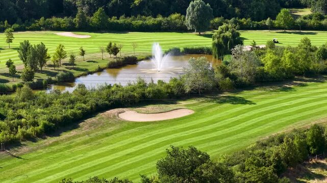 Aerial view of Magdeburg golf course shows striped fairways, golfcar, sand bunkers, pond fountain dense woodland. Summer landscape combines sport, water, manicured lawns and lush greenery