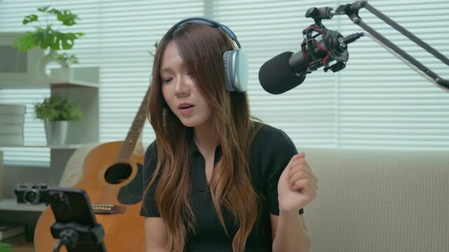Asian female influencer smiles brightly and happily to live singing on music livestream podcast. Concept of record cover song Freelance artist working from home ,social media creators.