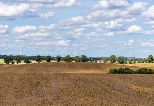 Weite Agrarlandschaft mit frisch gepfl&uuml;gtem Acker und Hochspannungsleitungen sowie Windkraftanlagen am Horizont, Uckermark, Brandenburg, Deutschland