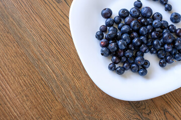 Top Down Shot of Ripe Dark Bilberries on White Plate Sitting on Wooden Surface © yaviki