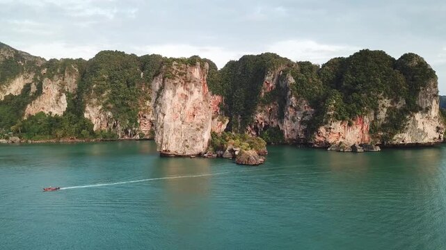 Aerial view of a long-tail boat cruising near the iconic limestone cliffs of Railay Beach in Ao Nang, Krabi, Thailand.