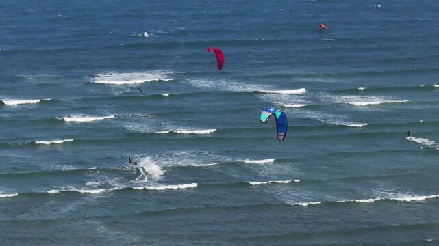 Aerial drone view of kite surfers riding the waves at My Hoa Beach in Vinh Hai, Khanh Hoa, Vietnam, showcasing a spectacular coastal landscape under bright sunlight. 
