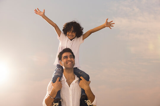 Boy sitting on his father's shoulder with hands outstretched 