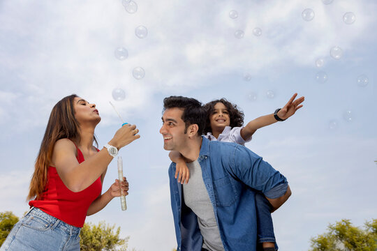 Happy parent with their son having fun with flying bubbles in the park