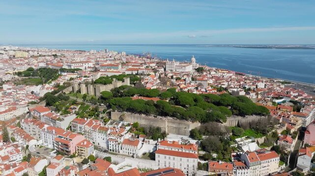 Slow panoramic drone shot of Castelo de Sao Jorge, Lisbon at midday. National Pantheon visible behind. Clear blue sky, bright sun. Portugal