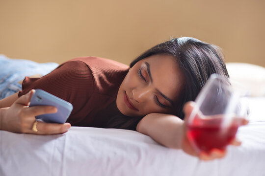 Young woman sleeping on bed with holding a glass of wine and Smartphone