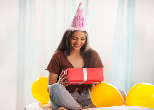 Portrait of a cheerful young woman wearing birthday hat and holding birthday gift in hand