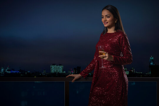 Cheerful young woman standing on terrace with a glass of wine during rooftop party