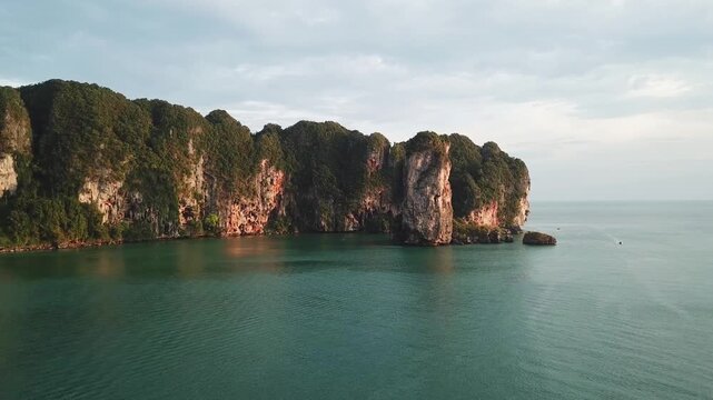 Aerial view of the dramatic limestone cliffs at Railay Beach, featuring lush vegetation and calm turquoise waters in Ao Nang, Krabi, Thailand.