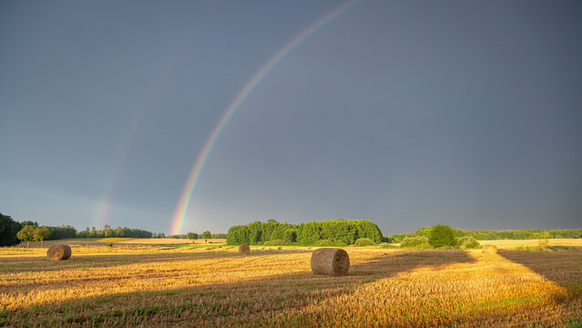 Countryside rainbow over hay bales after a sunlit rainstorm.