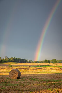 Hay bales in a countryside field beneath a sunset rainbow.
