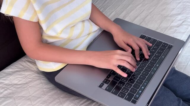 High angle shot of girl typing on laptop while sitting on bed, distance learning, digital homework, screen time
