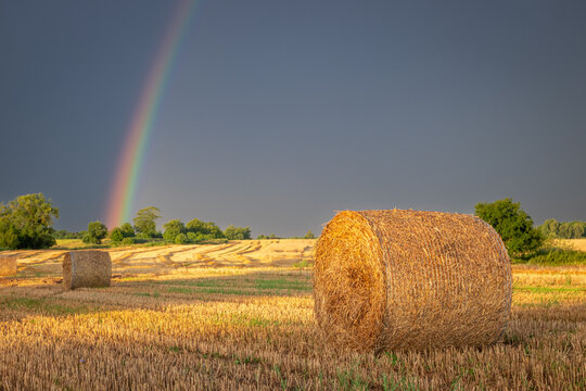 Golden hour rainbow over hay bales in a rain-freshened field.