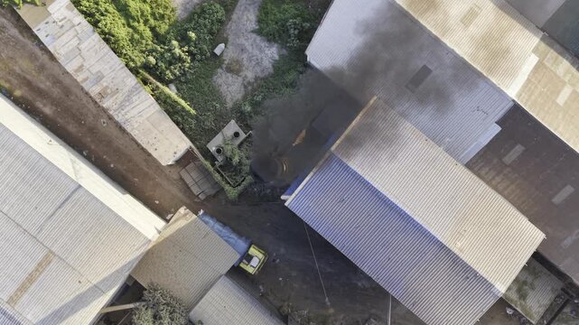 Aerial footage of an industrial smokestack releasing smoke above green farmland, trees, homes, and rural landscape, 