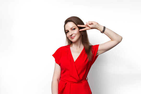 Young smiling girl in red dress showing peace gesture isolated on white background.