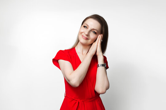 Young girl in red dress doing sleep gesture with hands on white background.