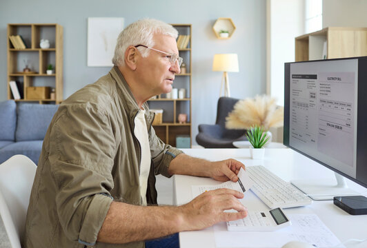 Senior man reviews invoice and bills on computer. He uses a calculator at home to verify utility charges, track expenses, and plan budgeting and finances. Clear bill payment budgeting concept.