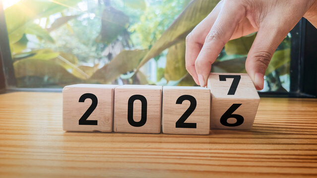 year transition wooden blocks changing 2026 to 2027. Close-up of wooden blocks showing year 2027 with finger changing block from 7 to 6. concept of time passing and upcoming year. copy space.