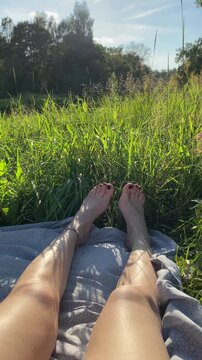 Tanned, slender women's legs in tall grass in the summer. Relaxing in the summer atmosphere, and enjoying the outdoors