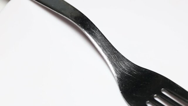A single metal fork lying on a white surface. Rotating in a circle