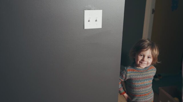 Smiling toddler holding a silver balloon peeking around a freshly painted dark grey wall