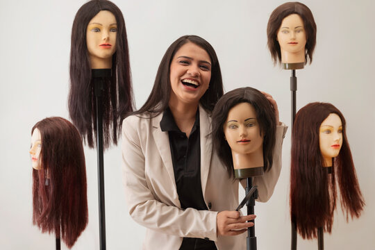 A HAIR STYLIST HAPPILY LAUGHING WHILE STANDING WITH DUMMY HAIR 