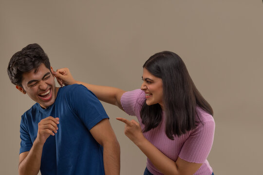 A YOUNG WOMAN PLAYFULLY REBUKING YOUNGER BROTHER