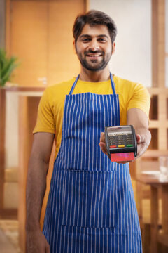 A CHEERFUL WAITER SHOWING CARD MACHINE FOR BILL PAYMENT