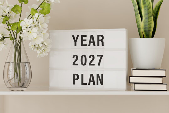 A lightbox displaying the words "Year 2027 Plan" on a shelf with books and plants.
