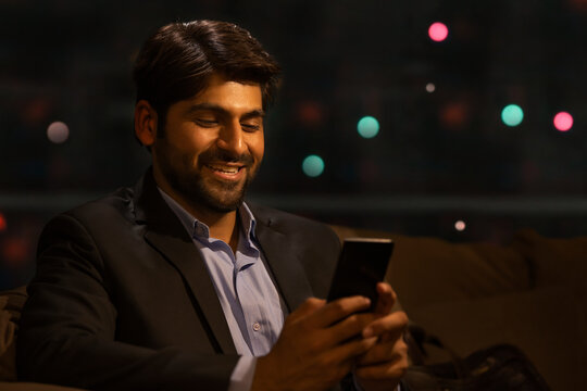 A YOUNG PROFESSIONAL HAPPILY USING MOBILE PHONE AT HOME