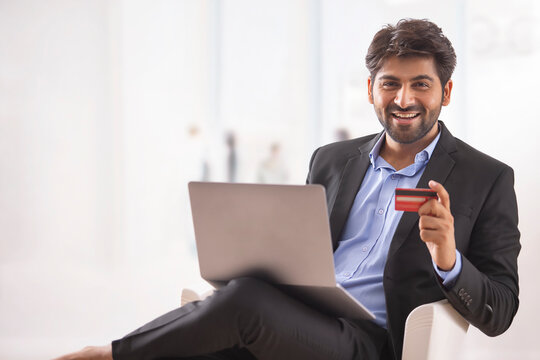 A YOUNG PROFESSIONAL LOOKING AT CAMERA WHILE DOING ONLINE TRANSACTION