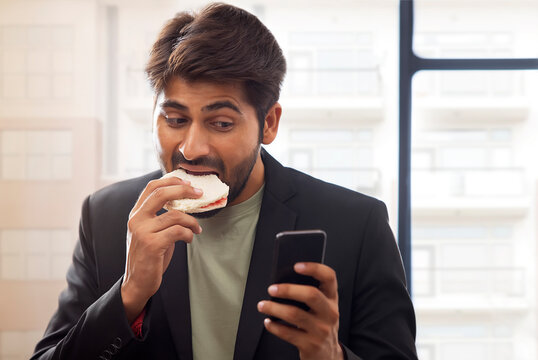 A YOUNG PROFESSIONAL BUSY WORKING WHILE EATING SANDWICH IN A HURRY