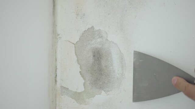 Slow motion close up of hand scraping peeling old paint and plaster off wall
