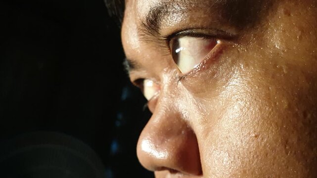 Extreme macro side view of an adult Indonesian Asian male eye looking sideways in dark low key lighting, capturing detailed brown iris texture, eyelashes, nose bridge, and subtle eyeball