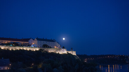 Petrovaradin Fortress stands illuminated under a bright full moon during the blue hour in Novi Sad, Serbia © Denis Renkas