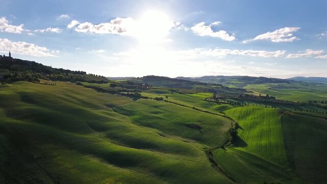 Aerial view of rolling green hills and sunlit landscape in Tuscany, Italy.
