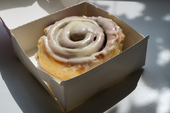 Fresh cinnamon roll with cream cheese frosting in takeaway cardboard box for bakery and dessert concept