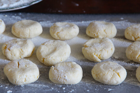 Homemade cottage cheese pancakes, syrniki being prepared on a floured surface, with raw syrniki dough portions ready for shaping and cooking.