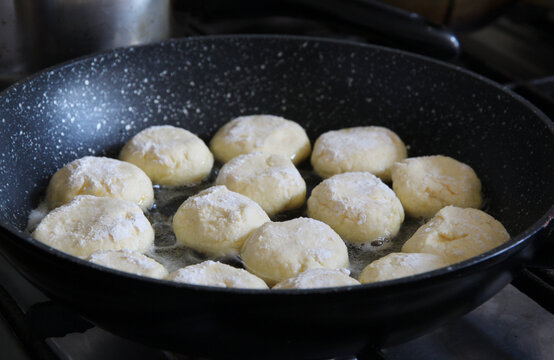 Homemade syrniki frying in a pan, cooking process of traditional cottage cheese pancakes dusted with flour and prepared for a delicious breakfast.