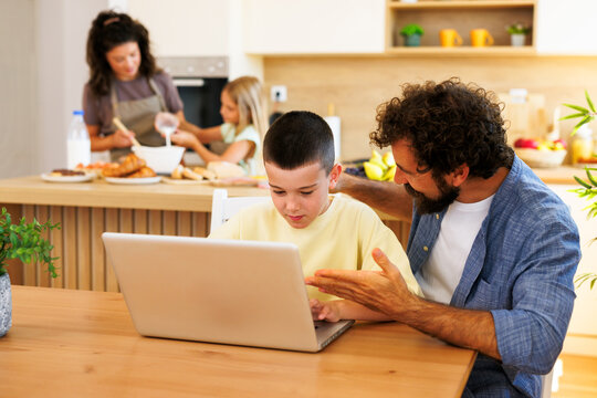 Father teaching son with laptop at kitchen table