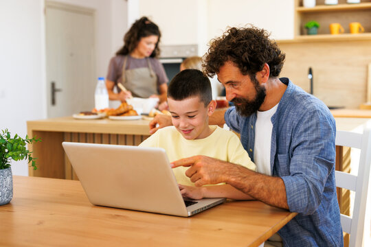 Father helping son learn on laptop at home